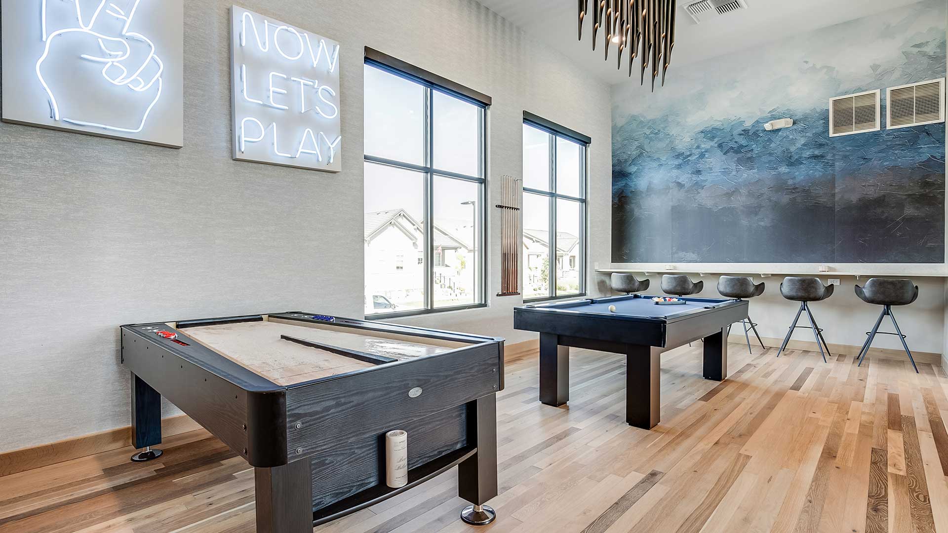 Modern resident game lounge at The Wright featuring billiards tables, shuffleboard, contemporary seating, and large windows with natural light.