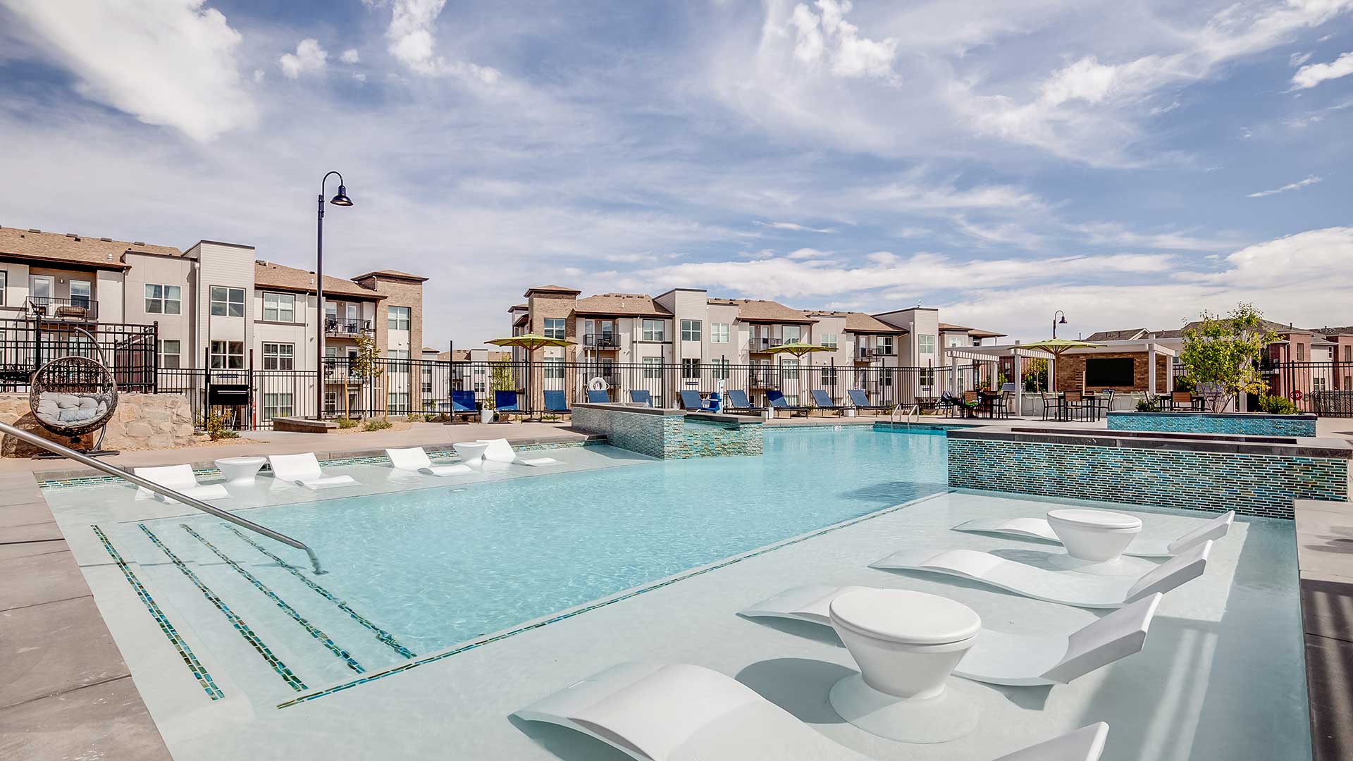 Outdoor pool and lounge area at The Wright in Centennial, Colorado featuring in-water seating, modern landscaping, and contemporary apartment residences in the background.