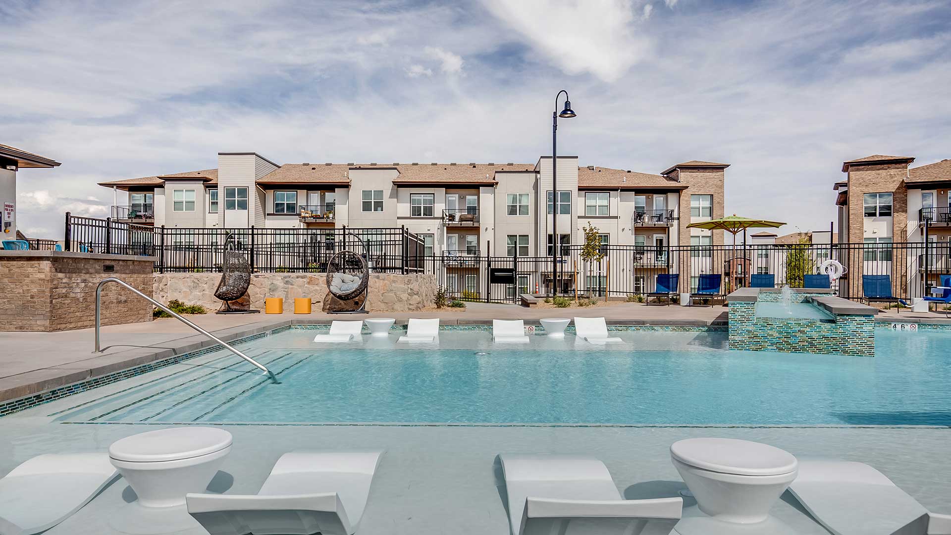 Outdoor resort-style pool at The Wright in Centennial featuring in-water lounge seating, poolside gathering areas, and modern apartment residences in the background.