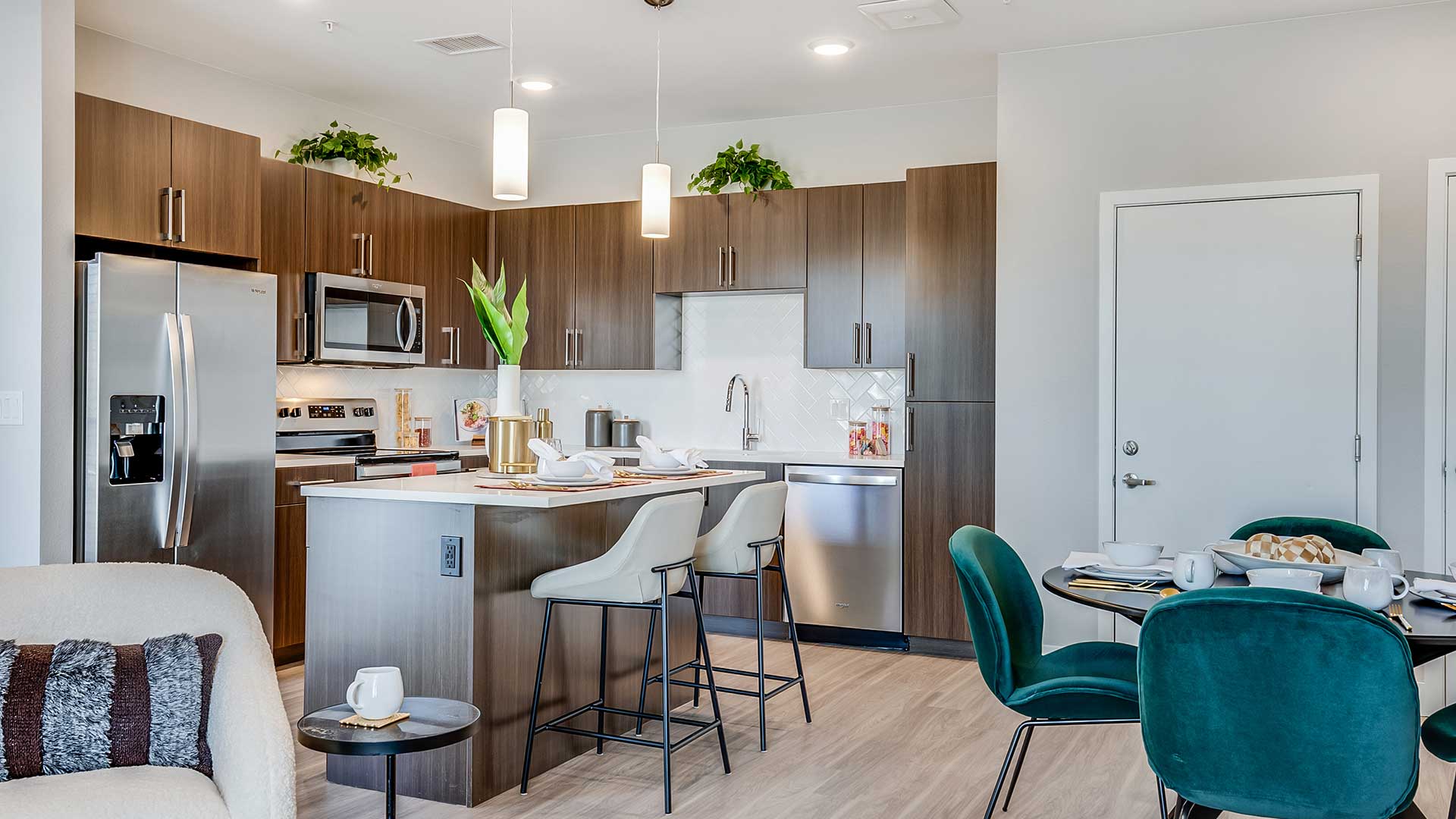 Modern open-concept apartment interior at The Wright featuring quartz countertops, stainless-steel appliances, wood-style flooring, and connected kitchen and dining spaces.