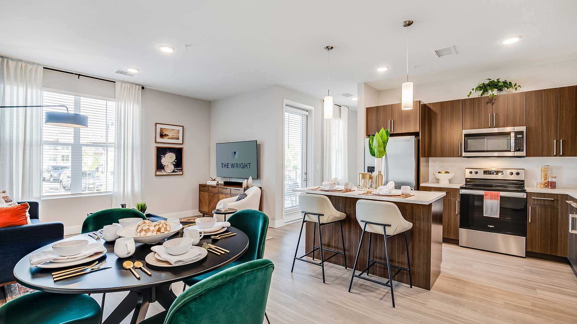 Open-concept apartment interior at The Wright featuring a modern kitchen with quartz countertops, stainless-steel appliances, wood-style flooring, and a connected dining and living area.