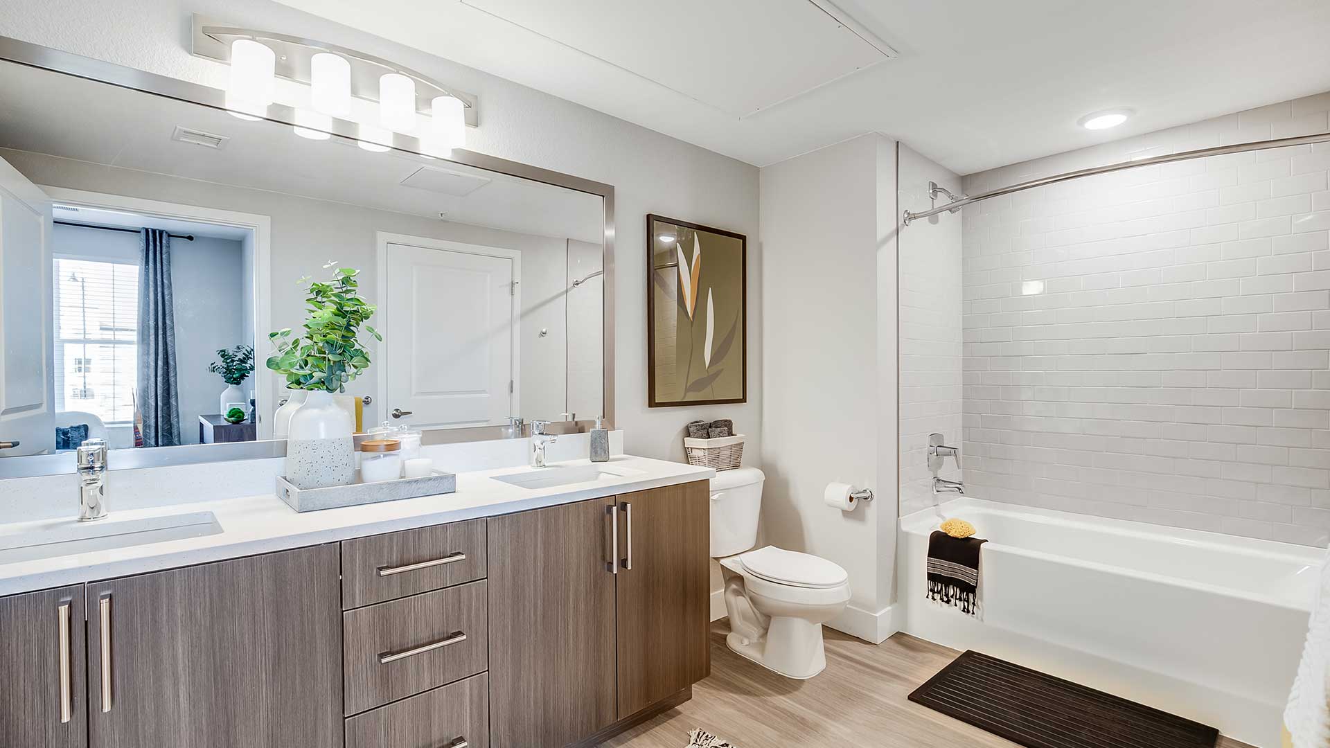Modern apartment bathroom at The Wright featuring quartz countertops, contemporary cabinetry, wood-style flooring, and a full tub and shower combination.