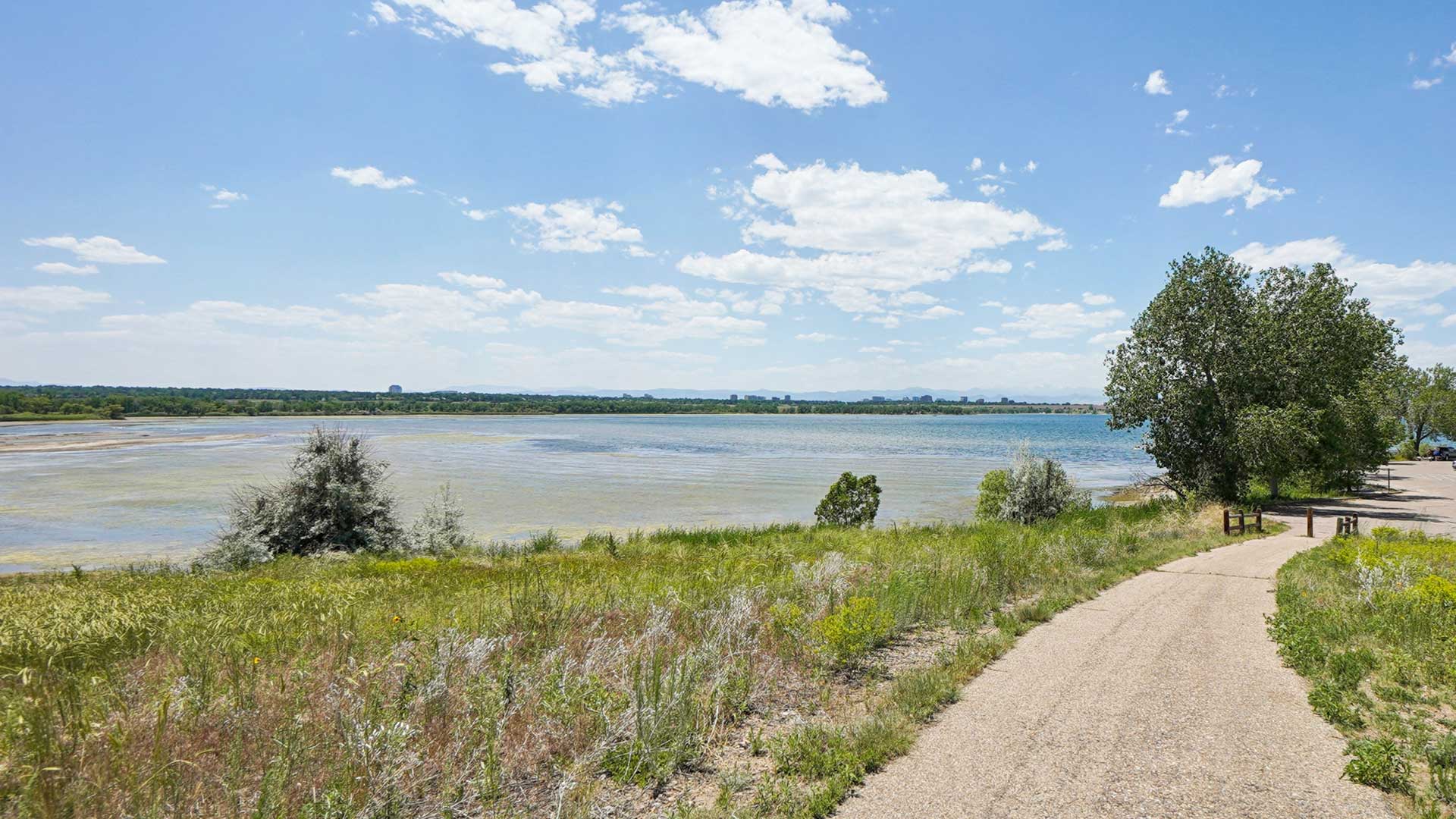 Scenic walking trail beside a lake near The Wright with open green space, water views, and mountain scenery in the distance.