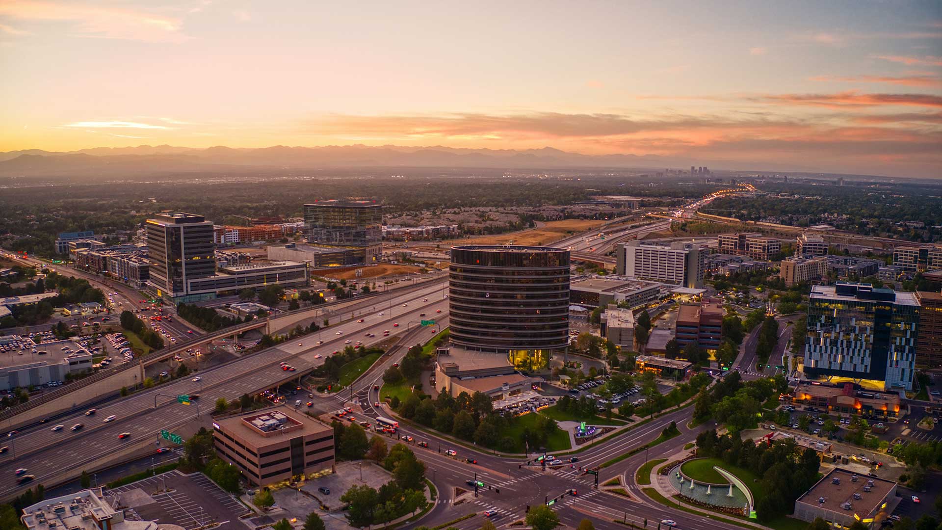 Aerial view of Denver Tech Center featuring office towers, major roadways, business districts, and mountain views near The Wright apartments.